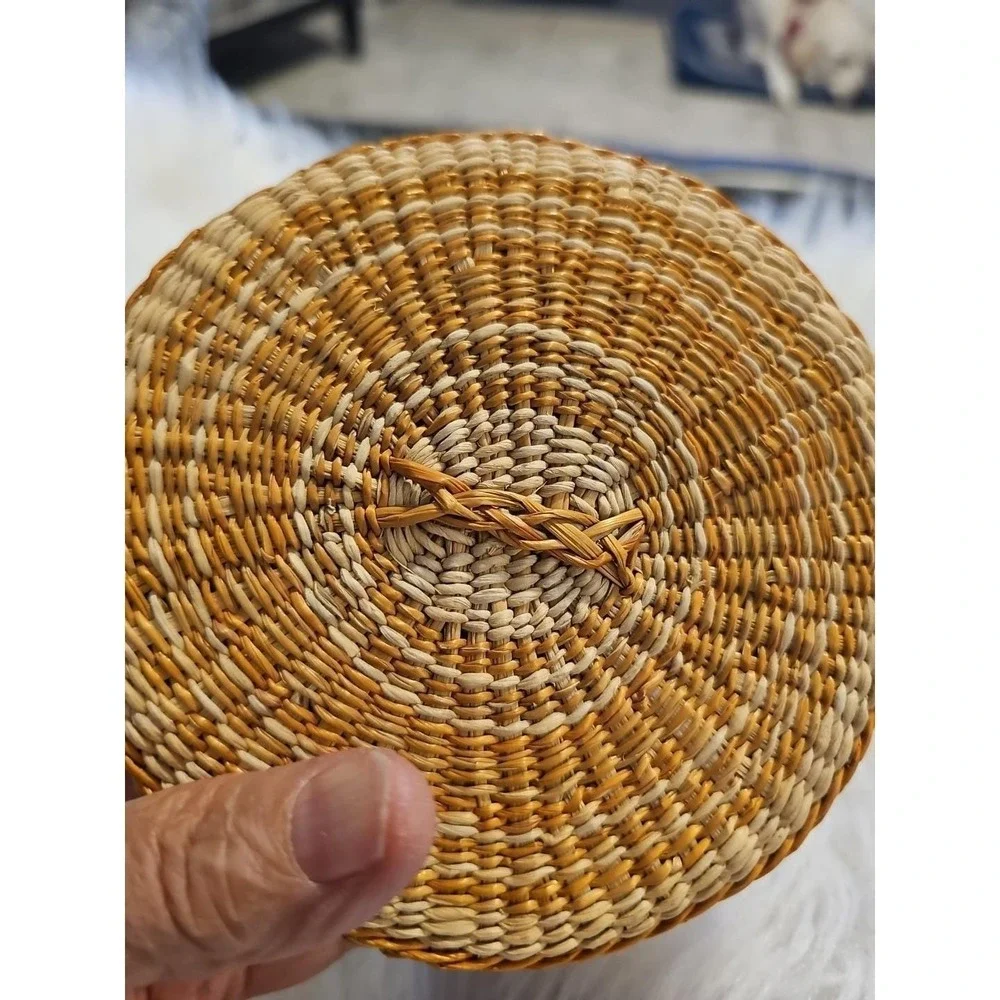 The image displays a‎ small, round, hand-woven basket with a lid, typically made